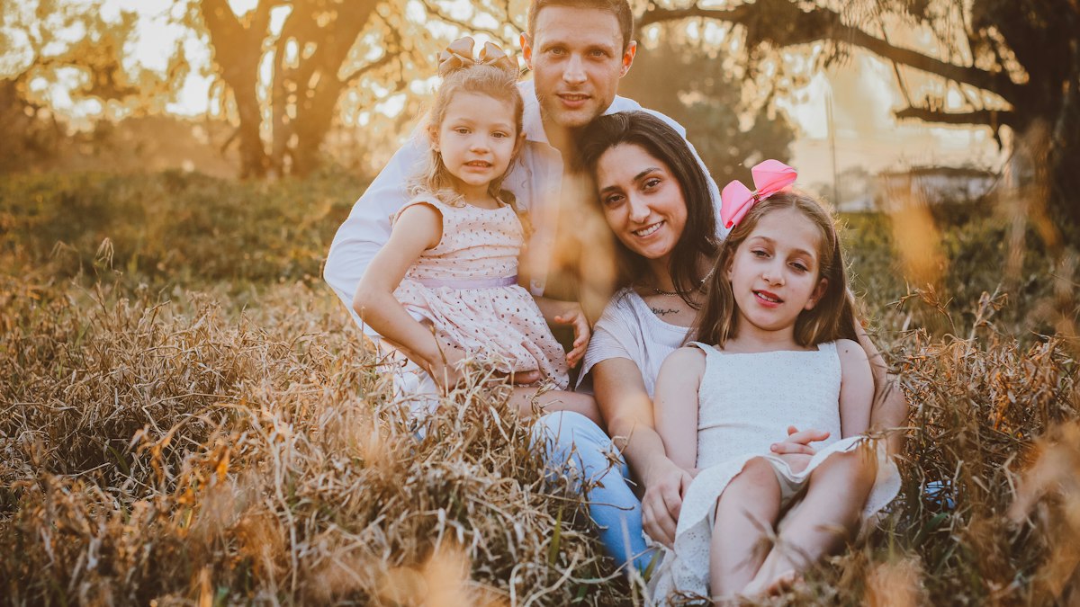 Smiling father with his two daughters sitting in a sunny field