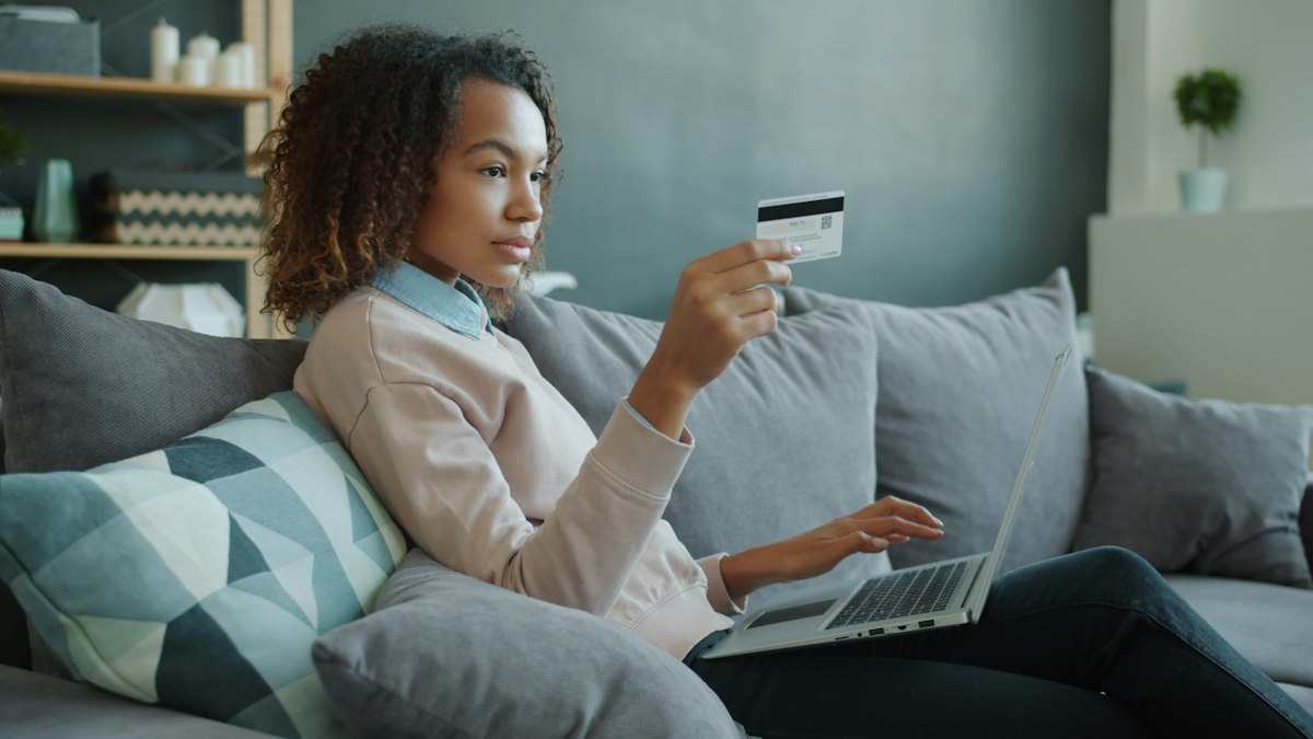 Young woman smiling on the sofa while checking her card and laptop