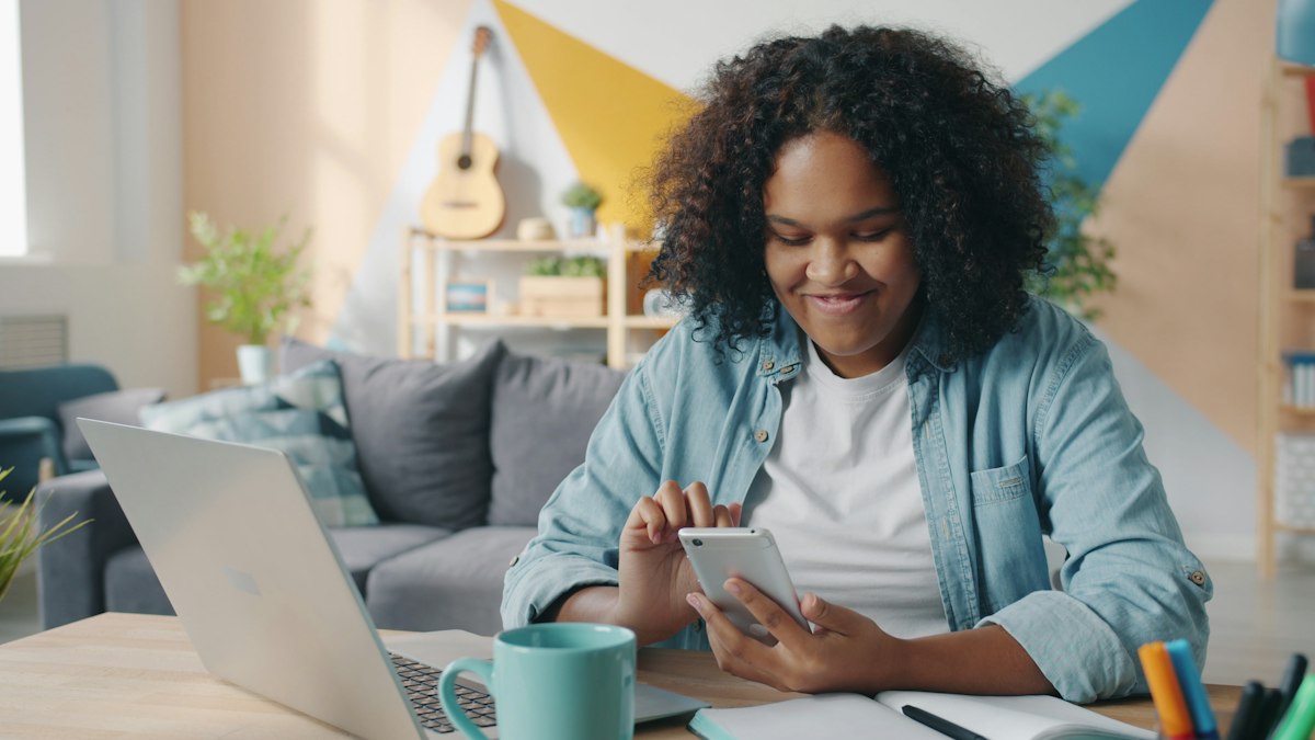Smiling student using her smartphone at her desk