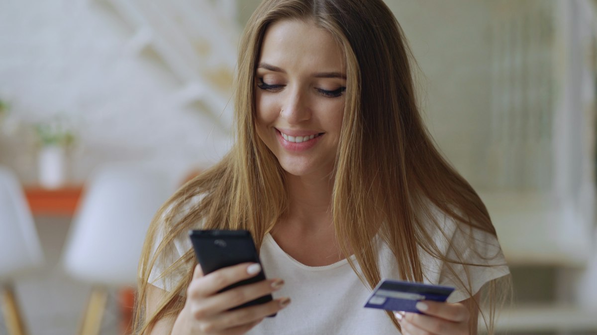 Young woman smiling while holding her first credit card and phone