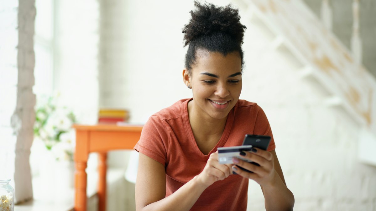 Young woman smiling while holding a credit card and her phone