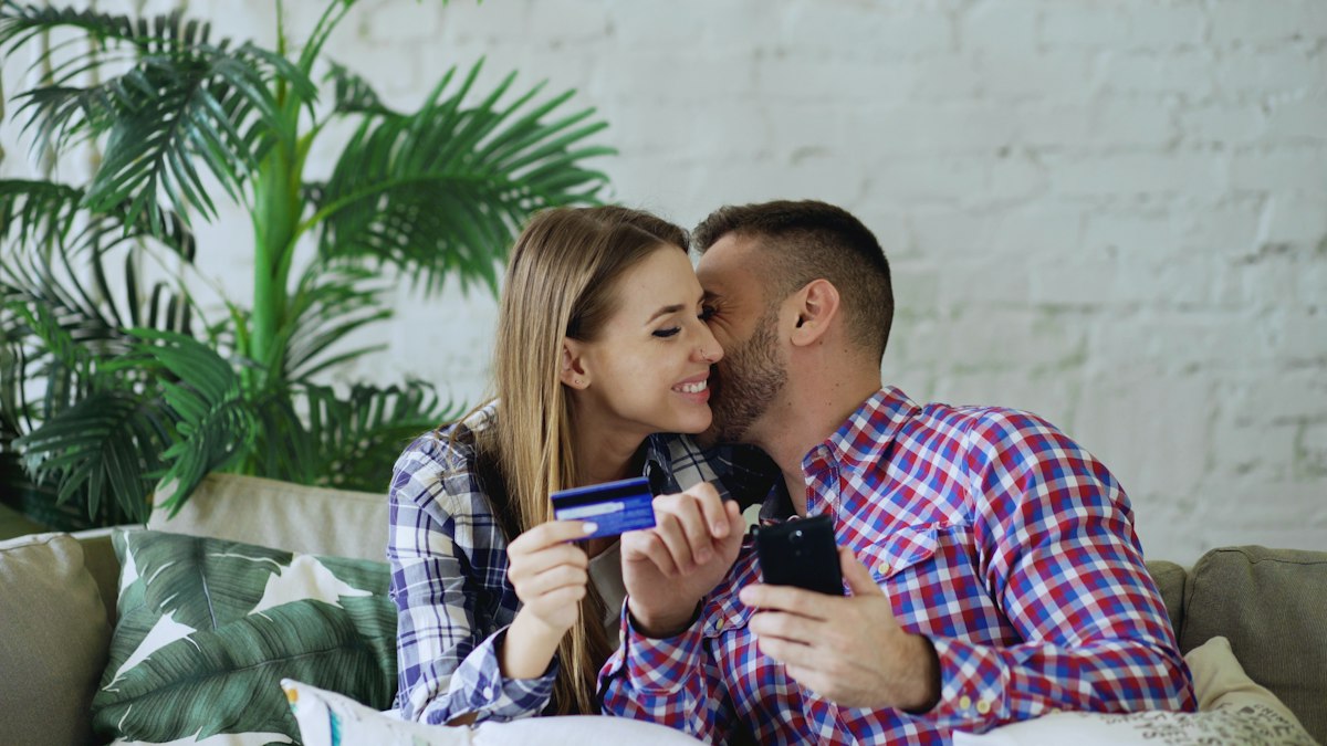 Smiling couple on the couch holding a credit card and phone